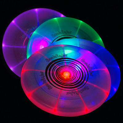 Nite Ize FLASHFLIGHT - LED Light Up Flying Disc. Four different colors of discs are shown glowing in the dark, leaning against each other.